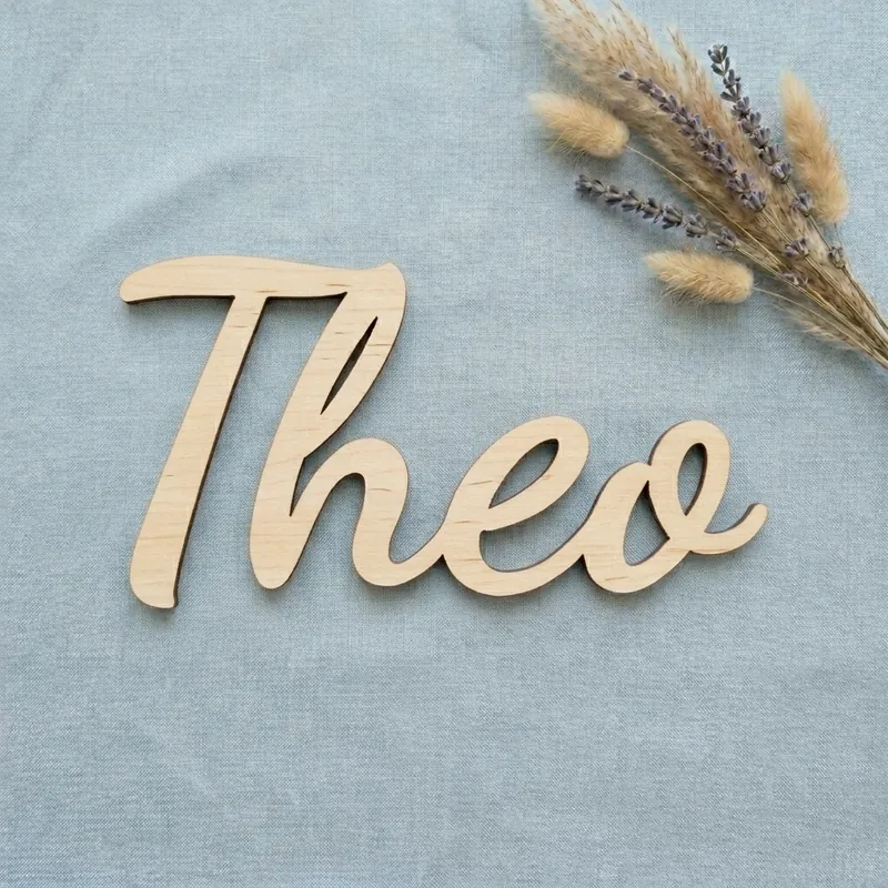 Wooden name sign reading Theo in the Swirly font, on pale blue linen